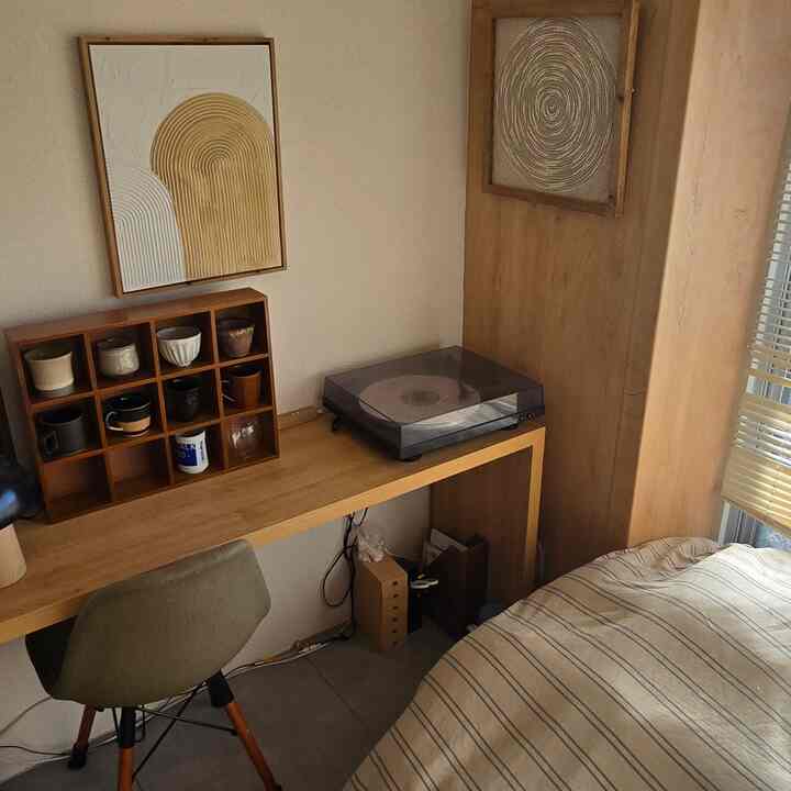 Wood tone and beige single household bedroom featuring a simple desk with a turntable and chair in a cozy home office setup