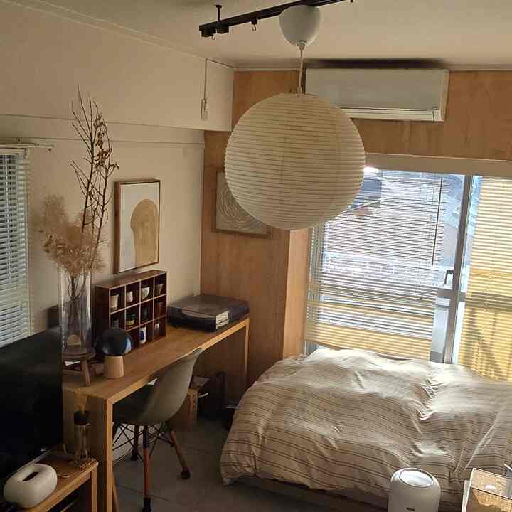 ベージュと木目調のワンルーム寝室、デスクとブラインドが配置された落ち着いた北欧風の雰囲気のあるインテリア