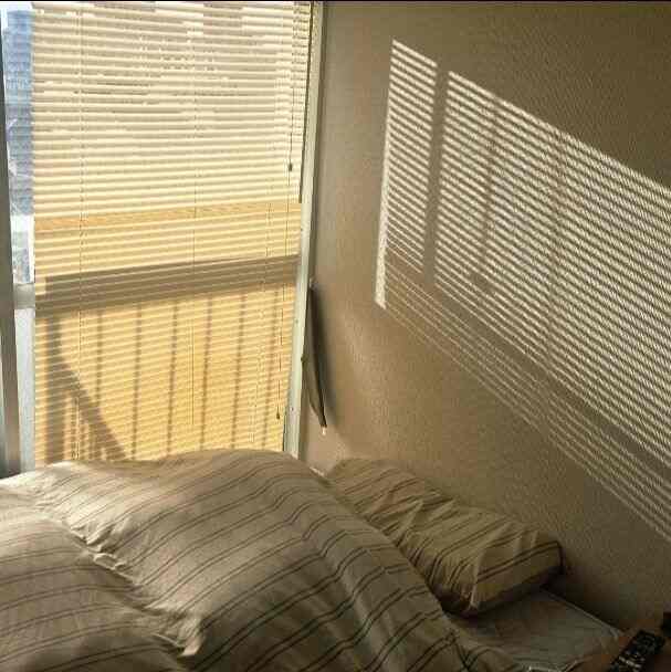 木目調のブラインドとストライプの寝具が配置された、温かみのある雰囲気のある寝室