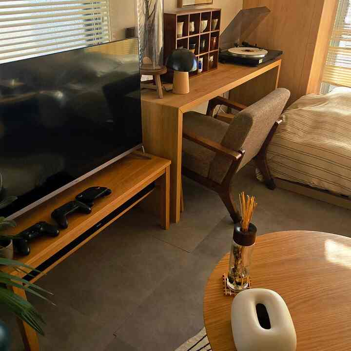 木目調の小さなリビング兼ホームオフィス、テレビ台とデスク、快適なアームチェアが配置されたモダンなインテリア
