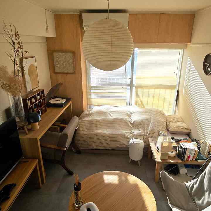 ナチュラルな木目調とベージュの色調の一人暮らし寝室、丸いコーヒーテーブルとペンダントライトが配置された雰囲気のあるインテリア