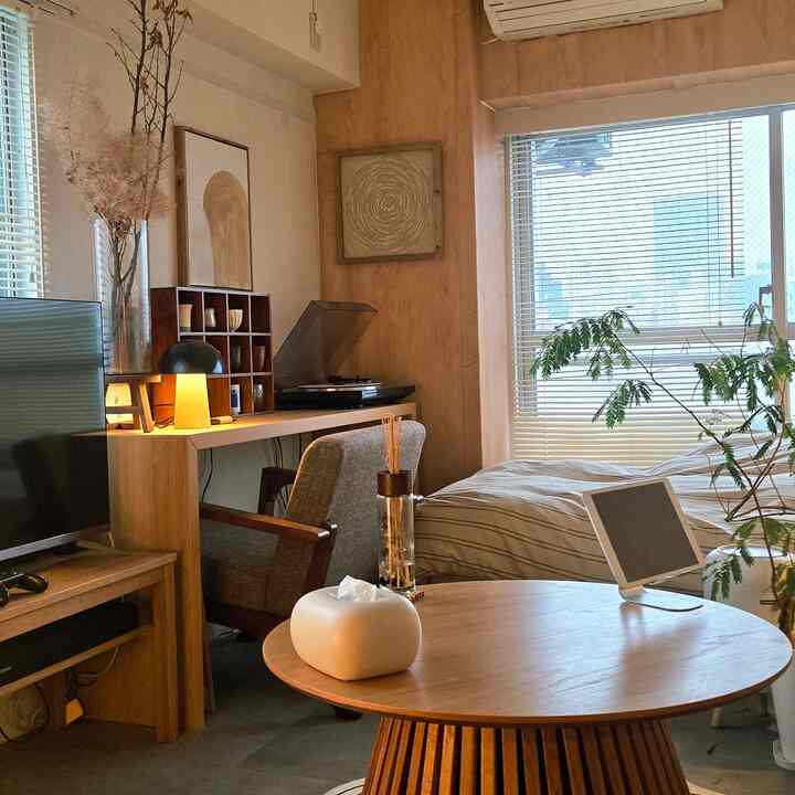ベージュと木目調が調和する一人暮らし用ワンルーム、デスクと植物が配置されたナチュラルな北欧風のインテリア