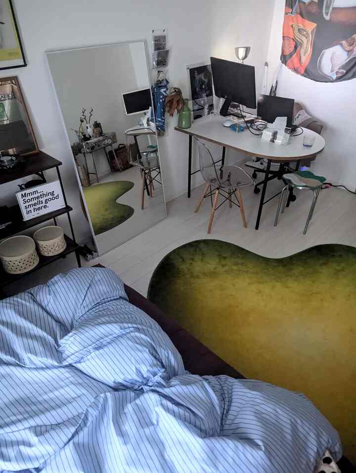 Modern bedroom with white floors and walls, blue striped bedspread, green gradient rug, large mirror and desk featuring a home office setup
