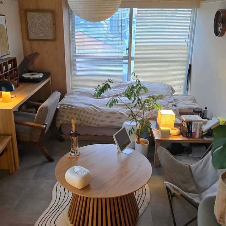 ライトブラウンの木製家具とナチュラルな色調の一人暮らし用寝室兼ホームオフィスの空間