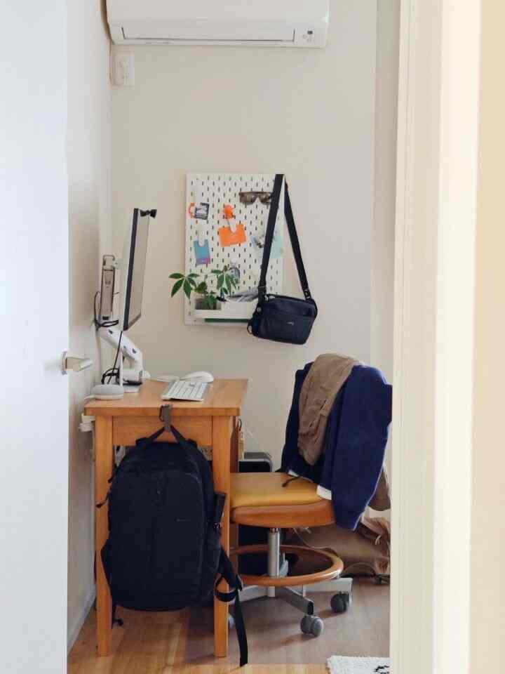 明るい木目調と白壁の寝室のホームオフィス、デスクと椅子、壁掛け収納が配置された清潔感ある空間