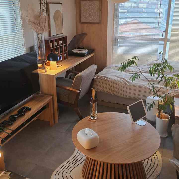 Natural color and wood tone studio apartment combining living and bedroom space featuring a round wooden coffee table, desk, and bed in cozy atmosphere
