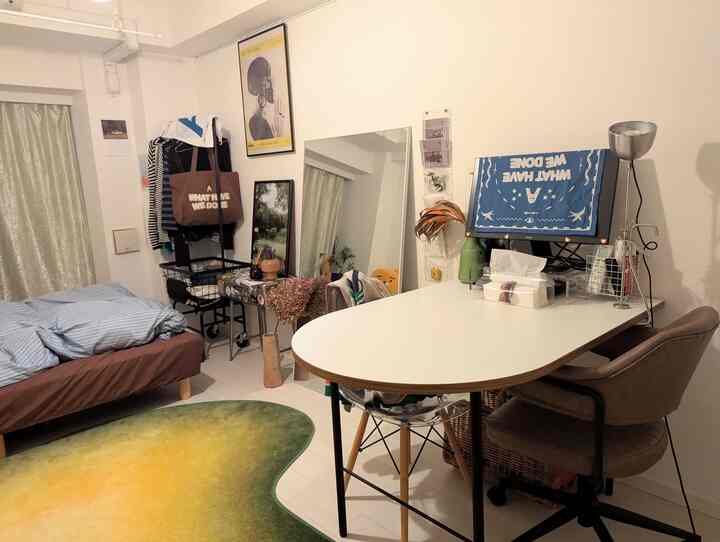 White and green toned studio apartment home office space featuring a large table, office chair, rug, and full-length mirror in a practical layout