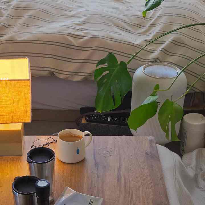 ナチュラルな木目調のテーブルと黄色いランプが置かれた、植物の葉がアクセントの雰囲気あるおうちカフェ空間