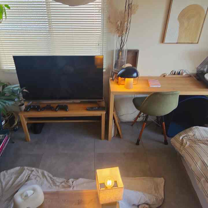 Wood tone and gray tiled living room with home office setup featuring TV bench, desk, and green chair in cozy space