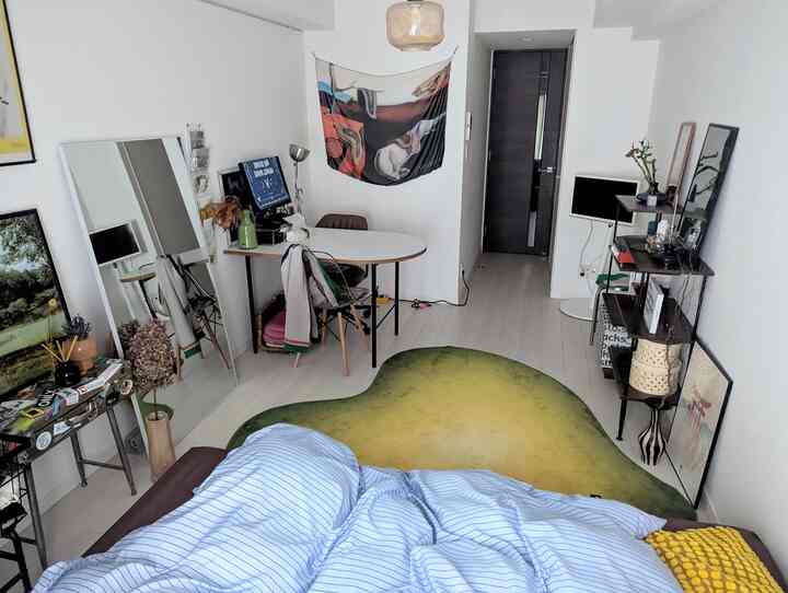 ホワイトとライトグレーのトーンが特徴のコンパクトな寝室、机と2脚の椅子、グリーングラデーションのラグが配置されたミニマルなホームオフィス空間