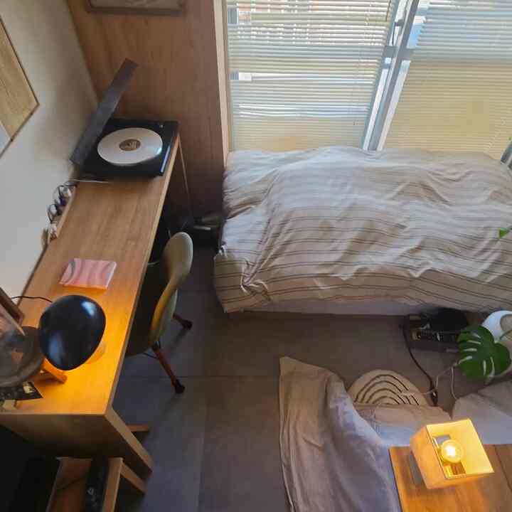 ナチュラルトーンのコンパクトな寝室、窓際に机とベッドが配置されたシンプルでモダンなインテリア