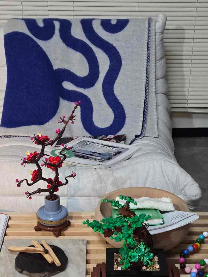 ナチュラルカラーとブルーが調和した一人暮らし用1LDKリビング、ソファには北欧柄のブランケットとオブジェの植物が配置された雰囲気のある空間