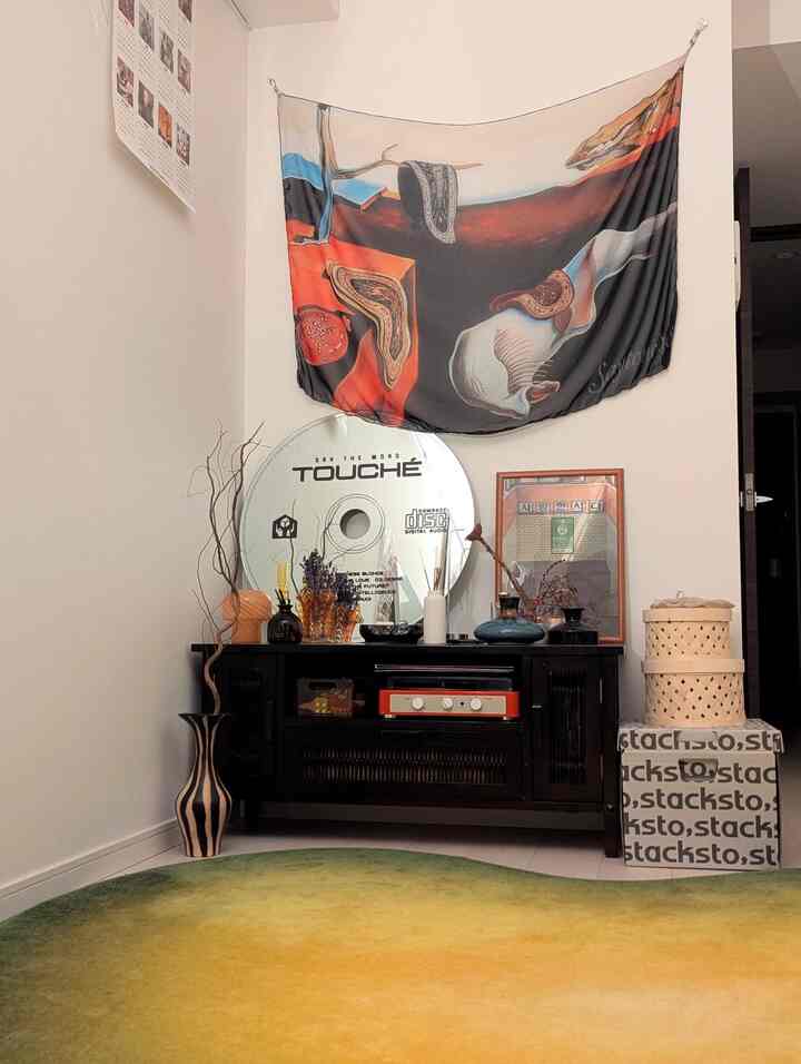 グリーンとイエローのグラデーションラグが敷かれたリビング、中央にダークウッドのサイドボードと壁にアートのファブリックポスターが配置された印象的な空間