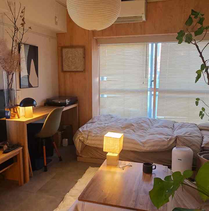 Natural warm-toned bedroom space featuring blinds, a desk, and a low table in a cozy studio apartment interior