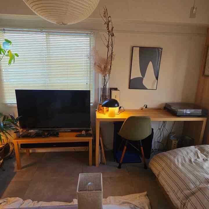 白と木目調が調和したワンルームの寝室、デスクとテレビ台が配置された温かみのある印象的な空間
