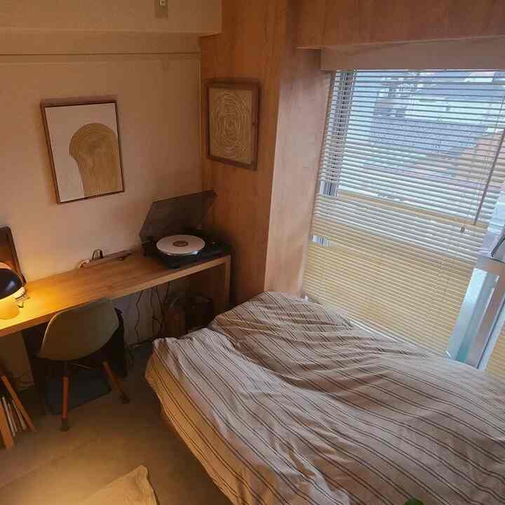 Beige wood-toned compact single-occupant bedroom featuring a bed, desk, and minimalistic simple design
