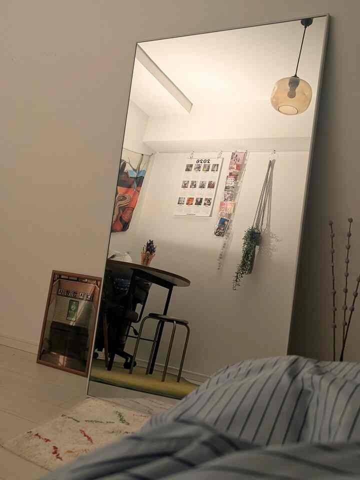 明るい白色調の部屋で、大きな全身鏡と丸いダイニングテーブル、メタルスツール、天井から吊り下げられたペンダントライトが配置されたシンプルなインテリア