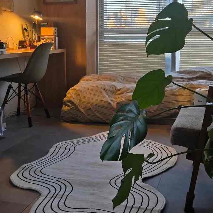 ベージュと黒の色調の寝室、ベッドとデスクが配置され、落ち着いたモダンな一人暮らし向けの空間