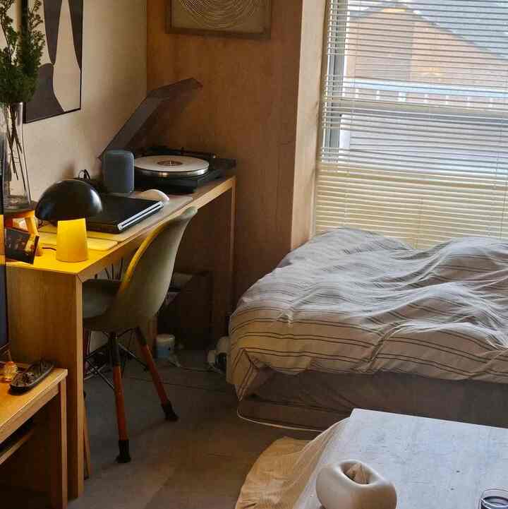 ナチュラルな色調の狭いワンルーム寝室、デスクとナイトテーブルが配置された落ち着いた空間