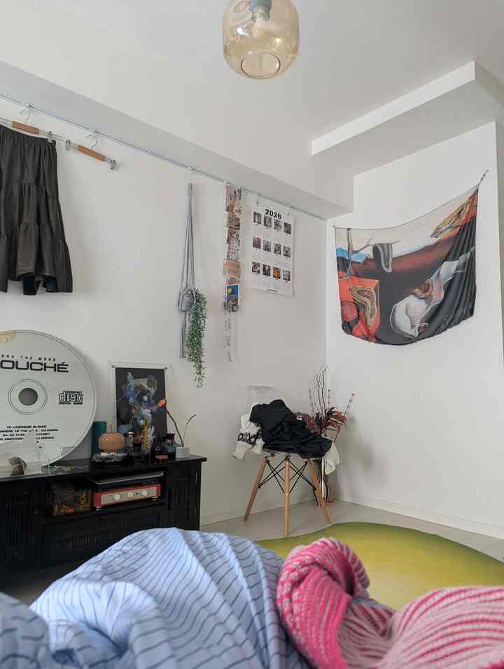 White-walled living room featuring a green gradient rug and fabric posters, creating a cozy and colorful atmosphere