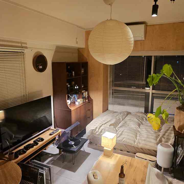 Cozy bedroom with warm wood tones and beige, featuring a bed, large pendant light, bookshelf, and wooden table lamp