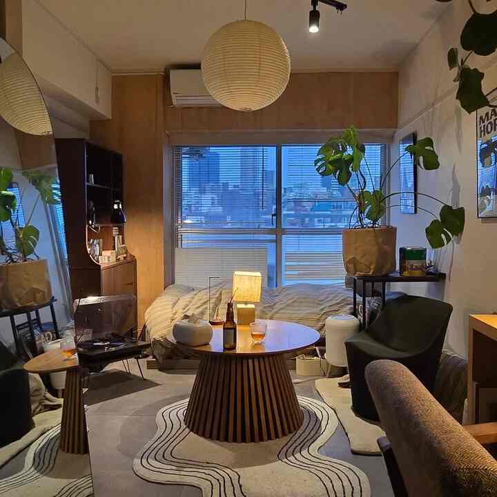 木目調のナチュラルカラーが印象的なワンルームのリビング兼寝室、丸いコーヒーテーブルと植物が配置された雰囲気のある空間