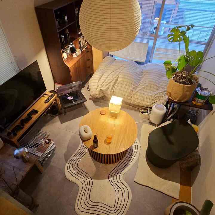 Natural modern tone small single household living room featuring a round coffee table, bookshelf, and pendant light with a cozy atmosphere