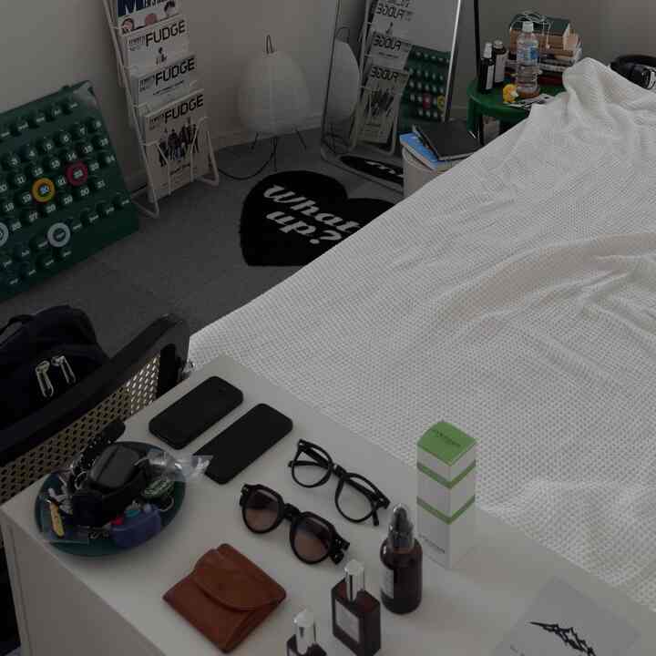 白い寝具のある一人用寝室、ナイトテーブル、鏡、黒のラグが配置された清潔感のある空間