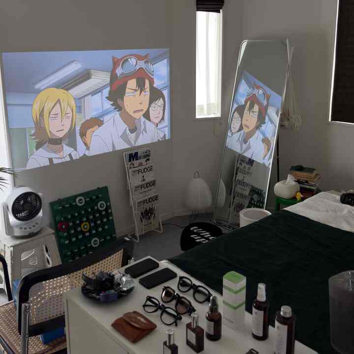 白い壁とダークグリーンのベッドカバーが調和したコンパクトな寝室、大型の鏡とプロジェクタースクリーンが配された印象的な空間