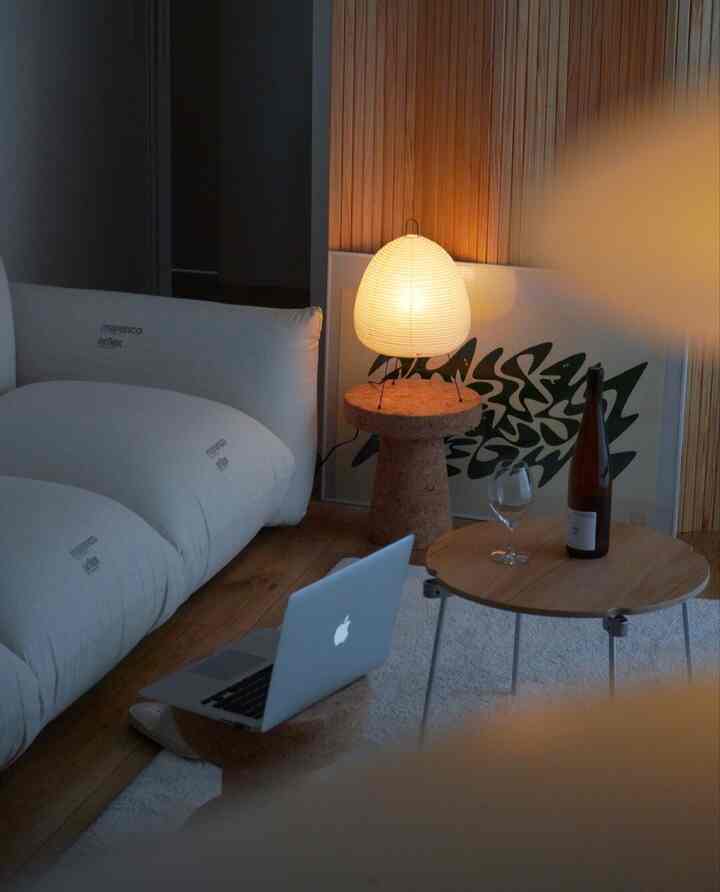 ナチュラルトーンのリビング、ベージュのソファとコルクテーブルに温かみのあるランプが置かれた雰囲気のある空間