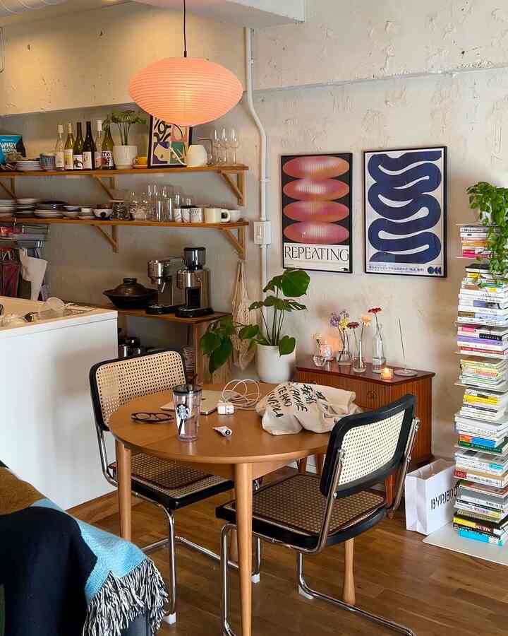 温かみのあるナチュラルカラーのリビング、丸い木製テーブルとラタンチェア、ポスターと本棚が配置された雰囲気のある空間