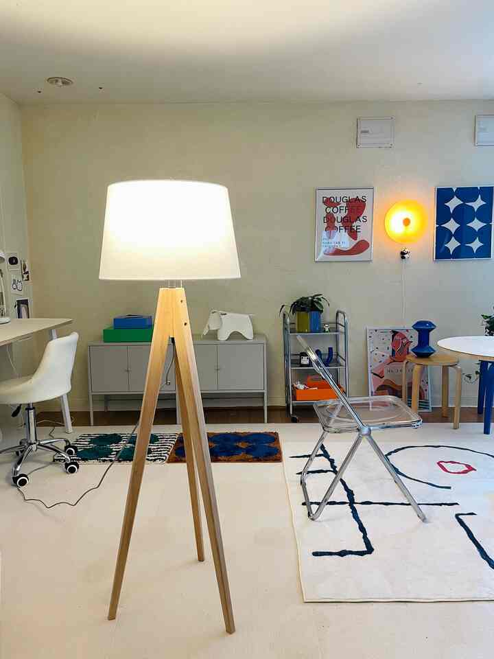 明るいベージュの壁と木製脚が印象的なフロアランプがある1DKリビング、北欧スタイルとカラフルなアクセントが調和した空間