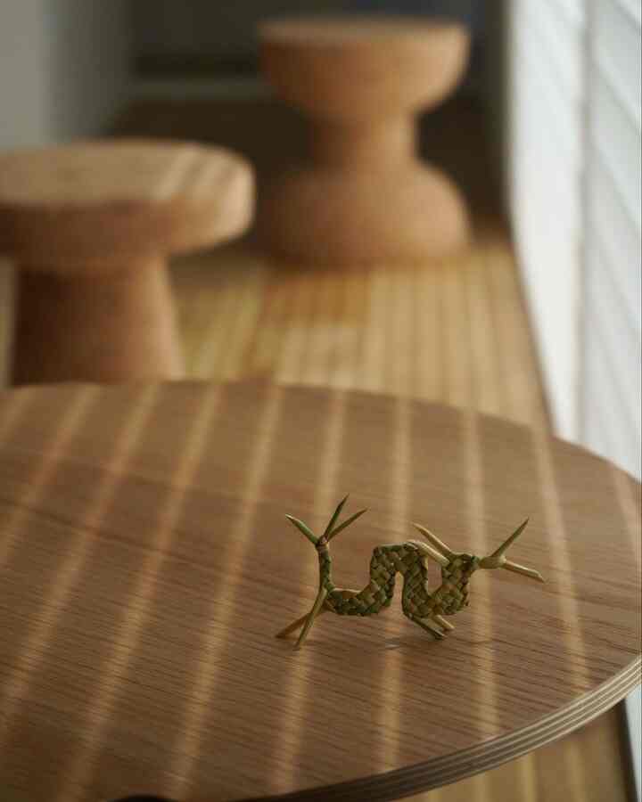 暖かい木目調の北欧スタイルリビング、丸い木製テーブルの上に稲藁で作られた小さな辰のオブジェが置かれた落ち着いた空間