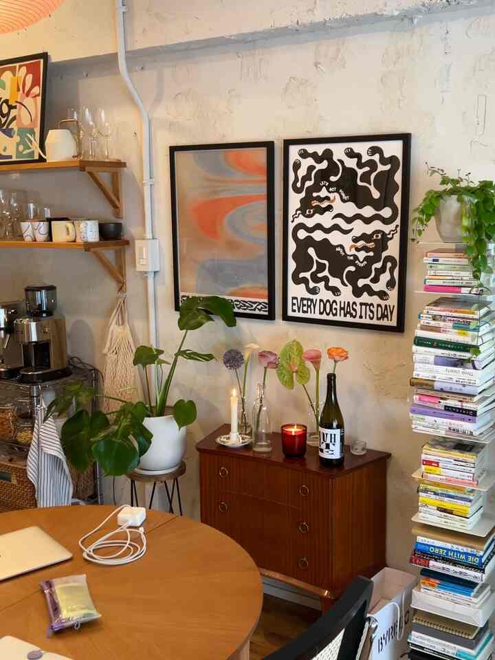 Brown and natural toned living room featuring a round dining table, posters, candles, and a tall bookshelf with cozy ambiance