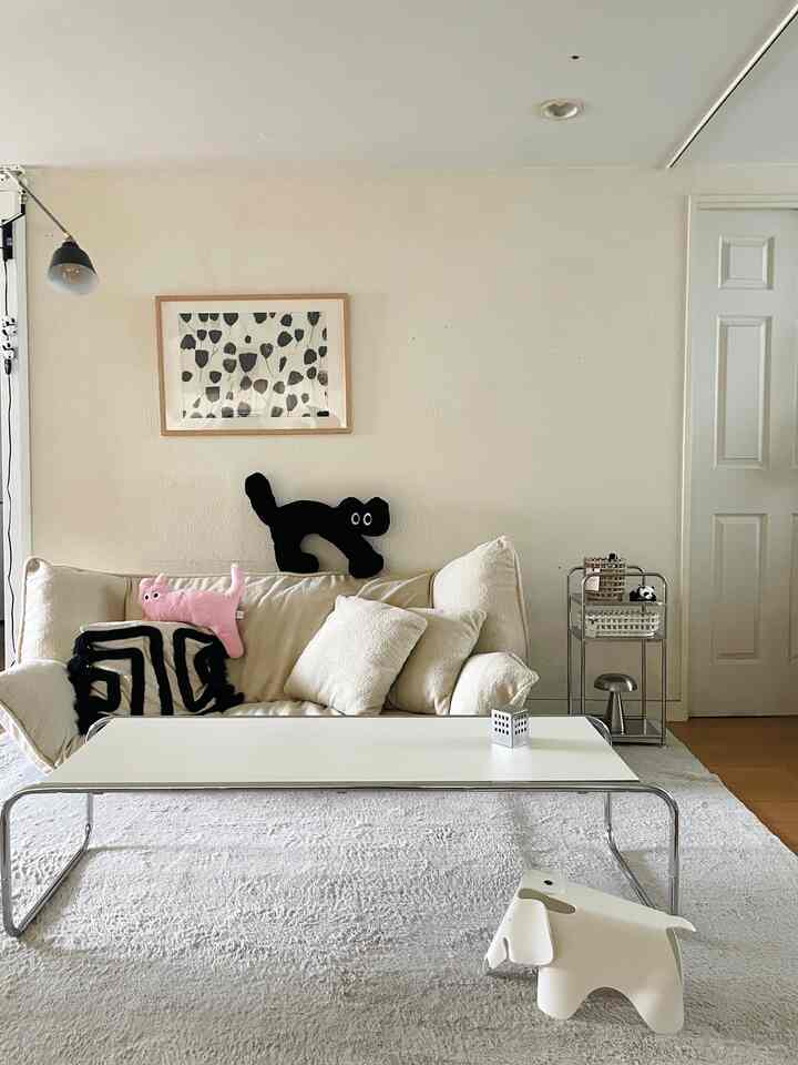 ホワイトとナチュラルカラーの1LDKリビング、ソファとコーヒーテーブル、猫のクッションが配置された雰囲気のある空間