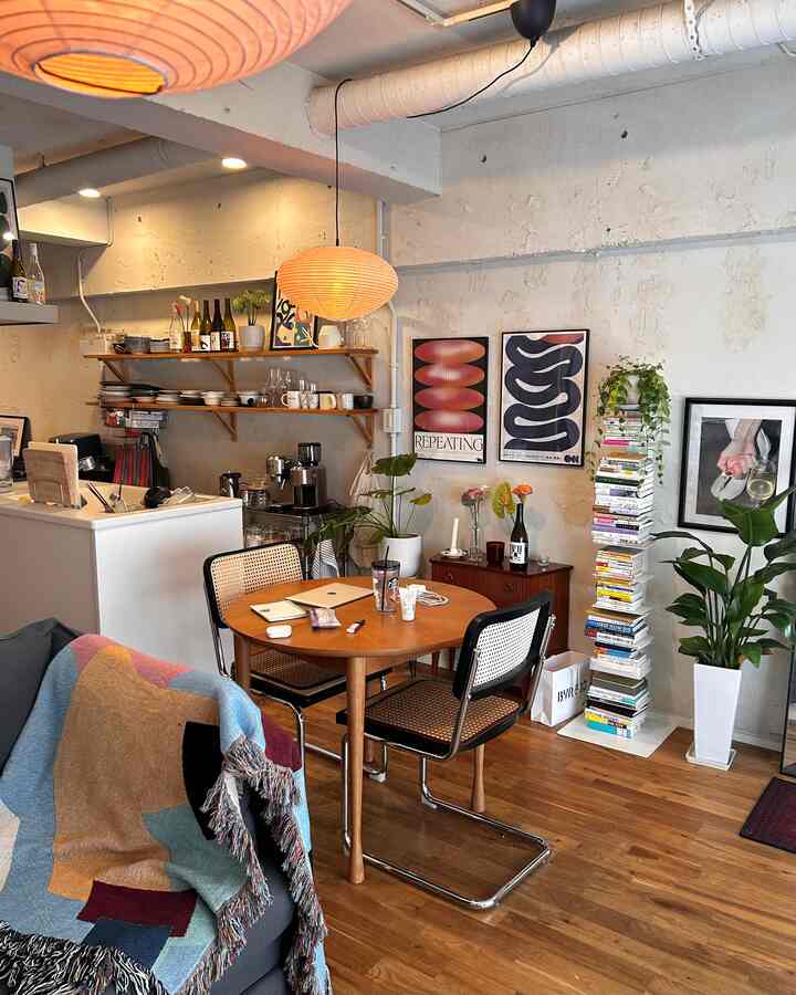 温かみのあるブラウン調とナチュラルスタイルのリビング、ラタンチェアと丸テーブル、本棚とポスターが配置された雰囲気のあるインテリア