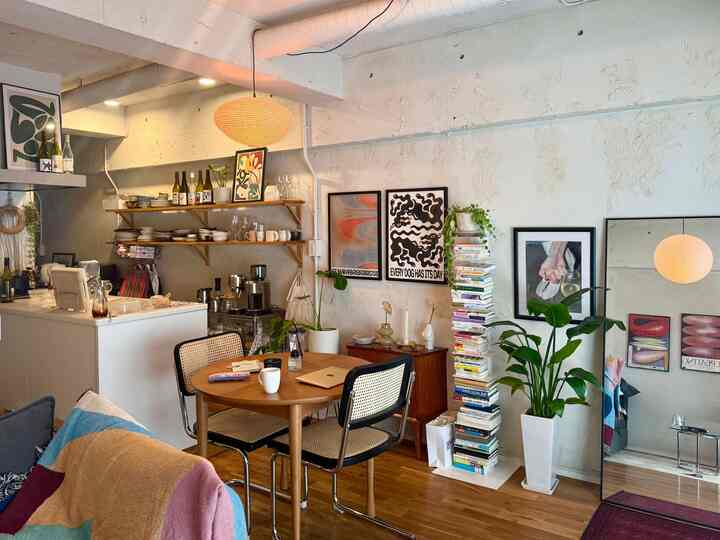 ブラウンの床と白い壁のリビング・ダイニング、ラタンチェアと丸テーブル、アートポスターや植物が配置されたナチュラルモダンなインテリア