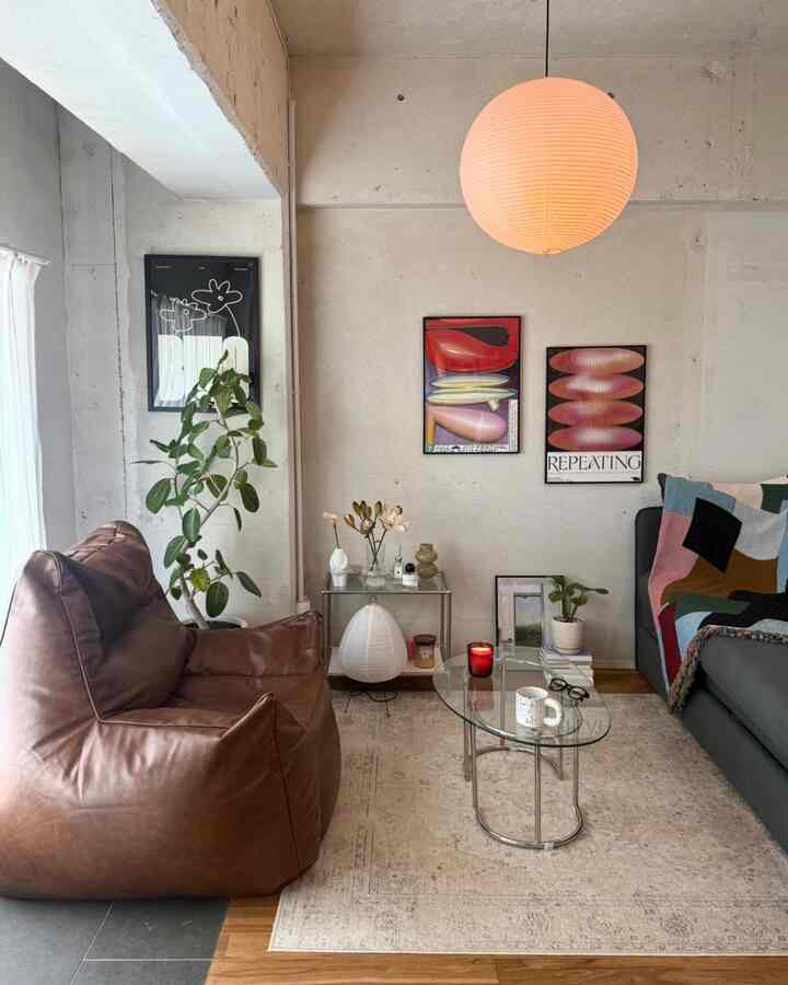 ブラウンのビーズクッションソファとグレーのソファを配したナチュラルトーンのモダンなリビング、アートポスターとガラスのローテーブルが印象的な空間