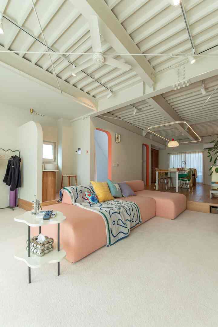 パステルピンクのソファと白いカーペットが印象的なオープンプランのリビングとキッチン、ナチュラルモダンな雰囲気のインテリア