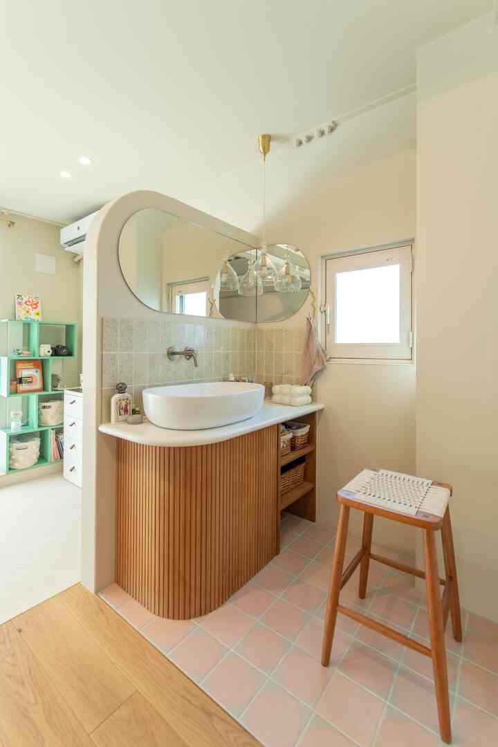 木目調とピンクのタイルが調和した玄関洗面スペース、L字型の鏡とスツールが置かれた雰囲気のあるインテリア
