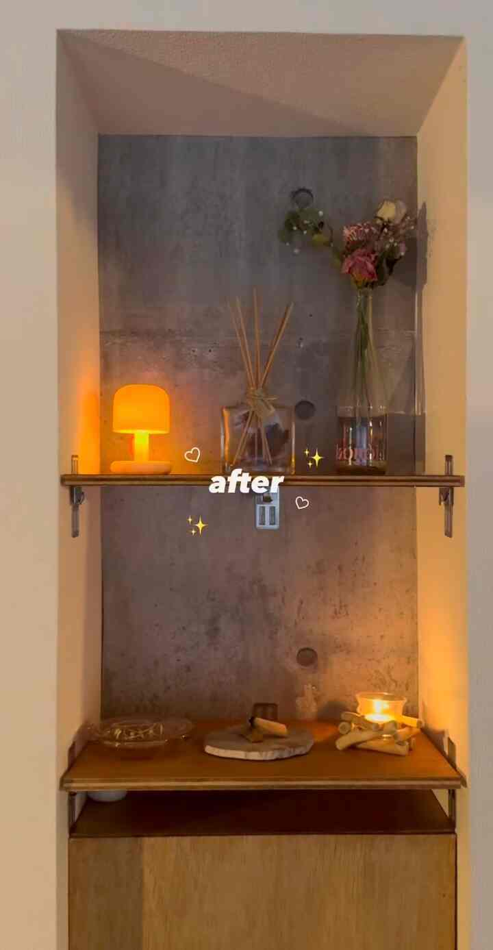 温かみのある木目調の棚とグレーのコンクリート壁、アロマディフューザーやキャンドルが配された雰囲気のあるインテリア