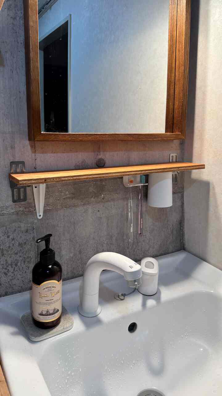 ナチュラルカラーとグレーのバスルーム、木製の鏡と棚が配置されたミニマルな空間