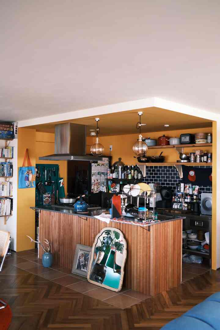 黄色い壁とナチュラルな木目調のキッチン空間、キッチンアイランドとオープンシェルフ、ペンダントライトが配置された雰囲気のあるレトロなインテリア