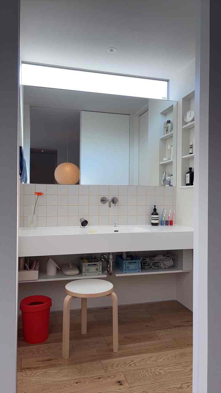 白と木目調のバスルーム、すっきりとしたスツールと収納スペースが配置されたミニマルでモダンなインテリア