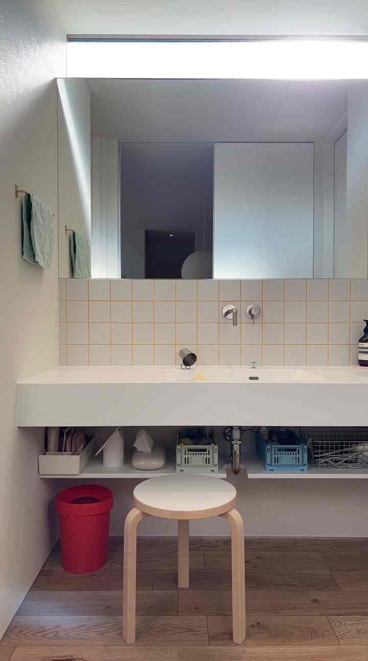 白と茶色のトーンのバスルーム、中央にスツールと大型の鏡が配置されたモダンな空間