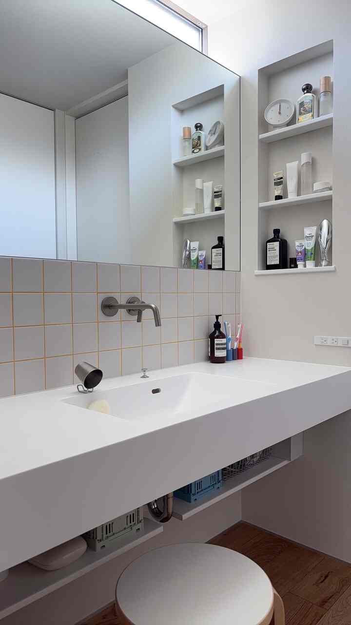 白を基調としたバスルーム、洗面台と棚に整然と配置された洗面用品があるモダンな雰囲気の空間