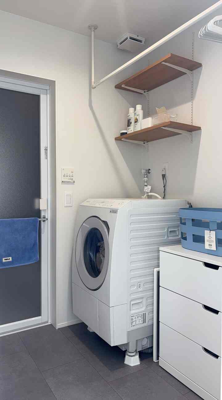 白を基調としたバスルーム、洗濯機と壁棚、収納キャビネットが配置された清潔感のあるインテリア
