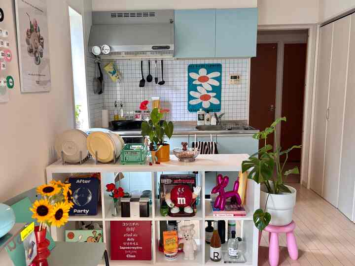 パステルブルーとホワイトのトーンのキッチン、イケアのKALLAX本棚と多様な小物が配置された雰囲気のあるオープンキッチン