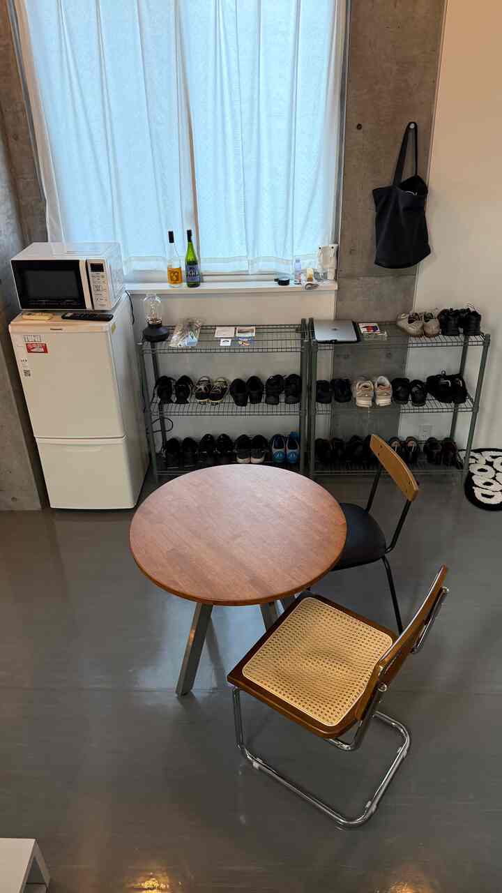 白い壁と茶色い木製ダイニングテーブル、多様な椅子が配置された狭いダイニング空間とシューズラックのある室内