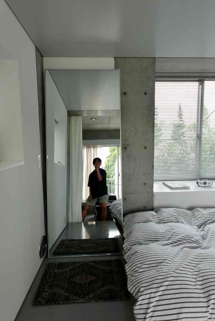 グレーと白を基調とした寝室、大きなイケアの鏡とストライプの寝具が配置された雰囲気のあるモダンな空間